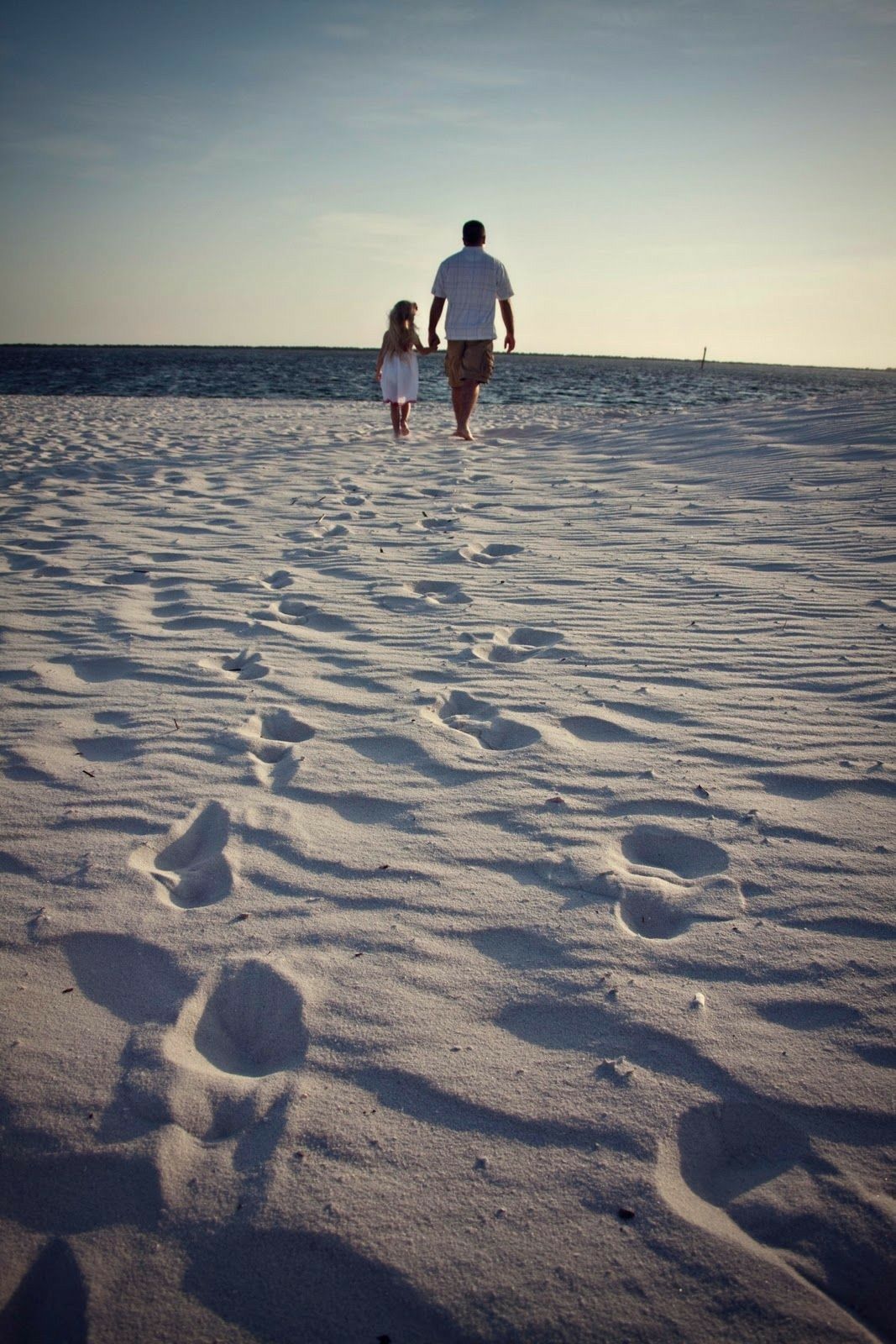 Hình ảnh một người đàn ông và con gái của mình đi dạo trên cát